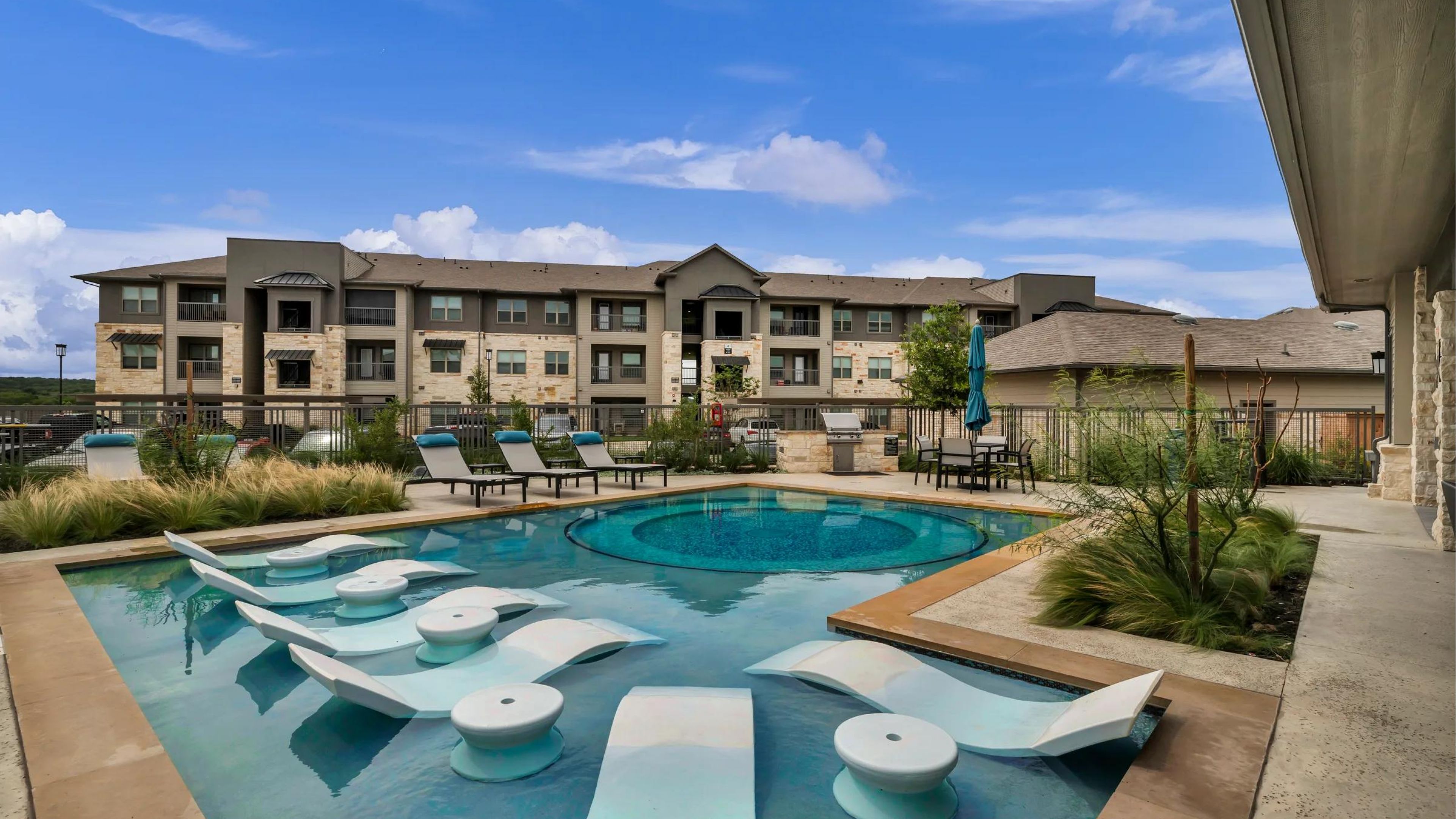 Hawthorne at Blanco Riverwalk modern apartment complex with a swimming pool, lounge chairs, and partly cloudy blue sky.
